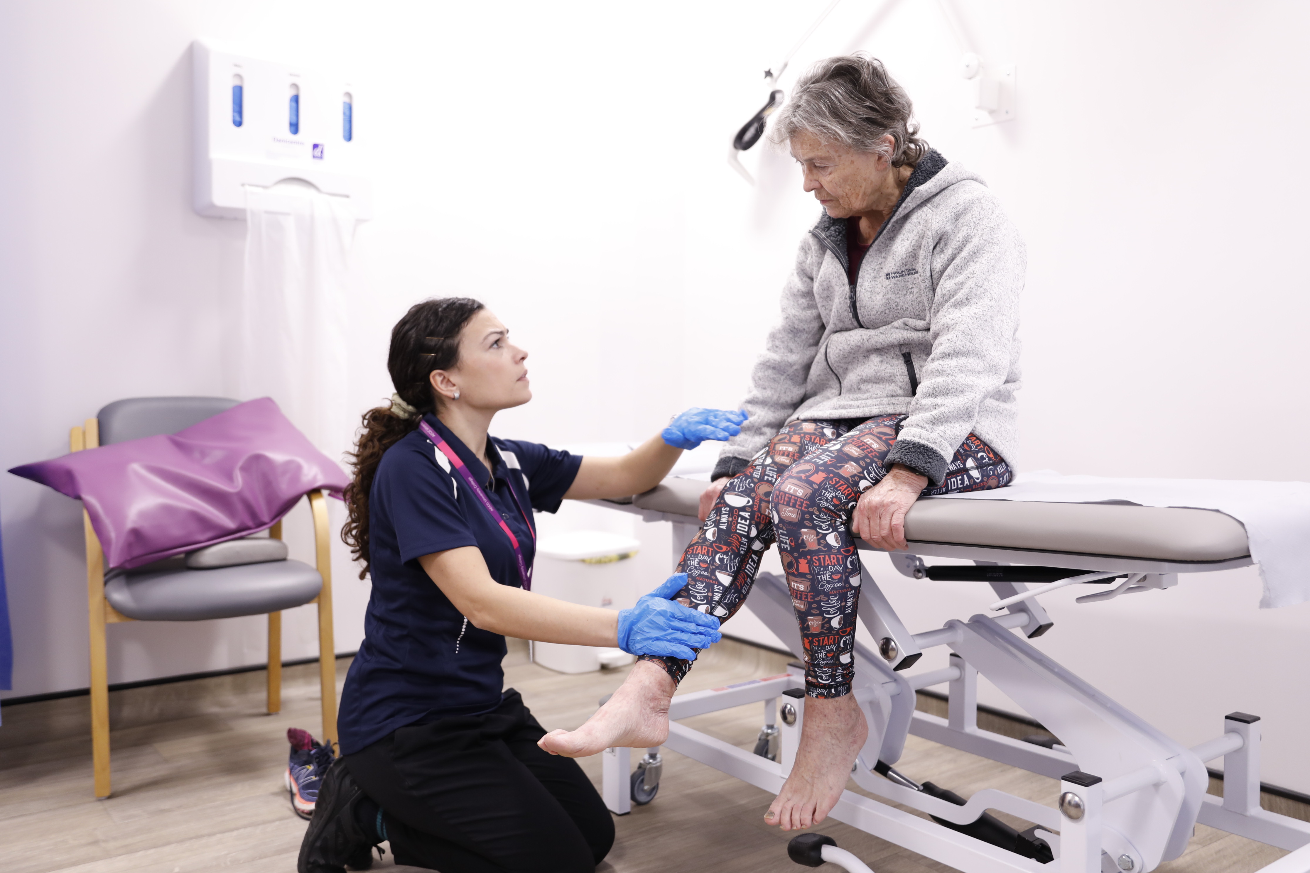 Physiotherapist crouched down looking intently up at patient on a physio bed, assessing her knee/leg