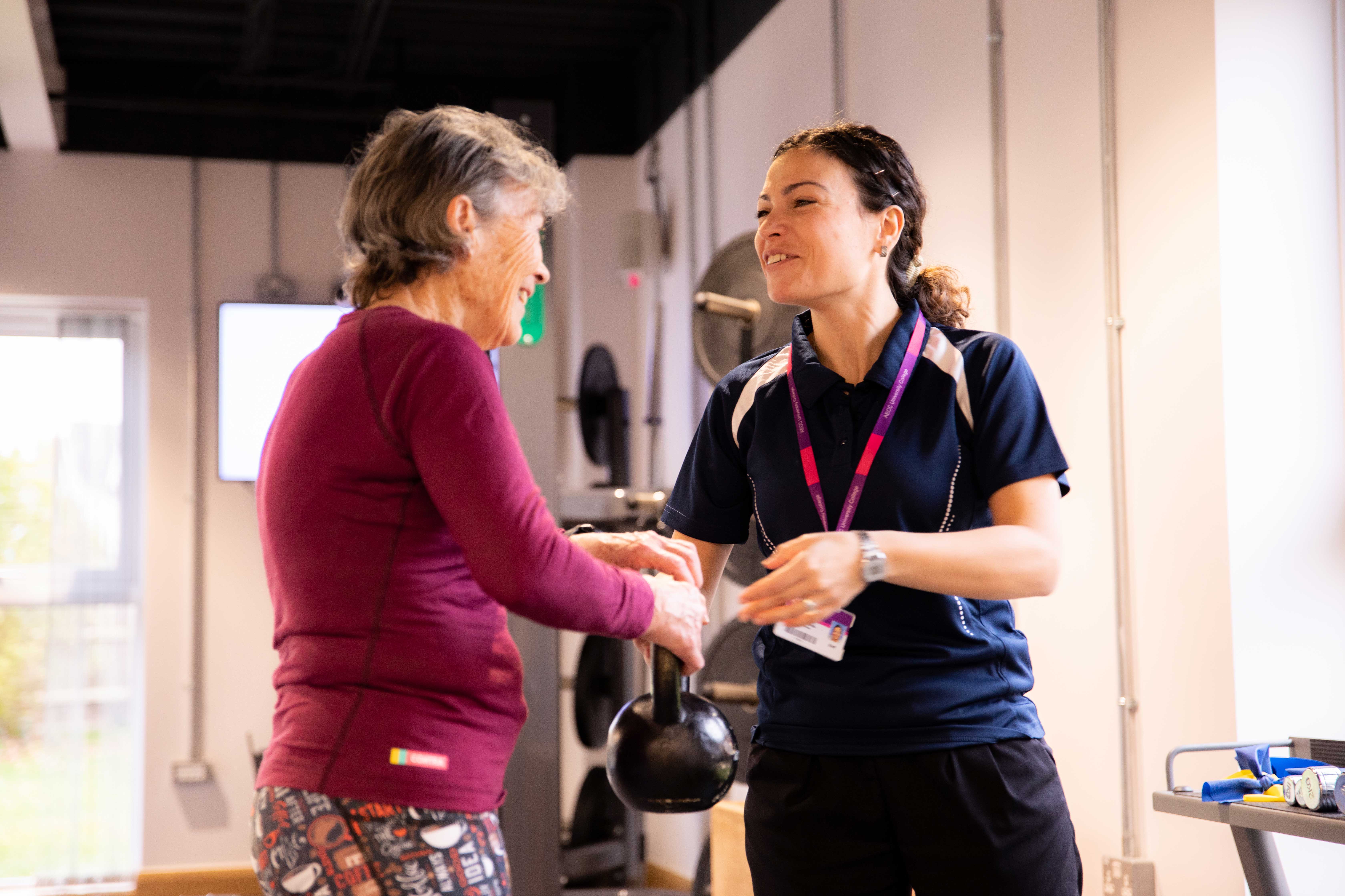 Physiotherapist handing an elderly patient a kettle bell during an exercise rehabilitation session